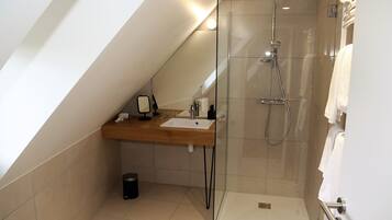 A modern bathroom with a glass shower enclosure, a wooden vanity, and a small trash bin.