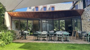 Un patio al aire libre con mesas y sillas, una terraza de madera y un edificio de piedra al fondo.