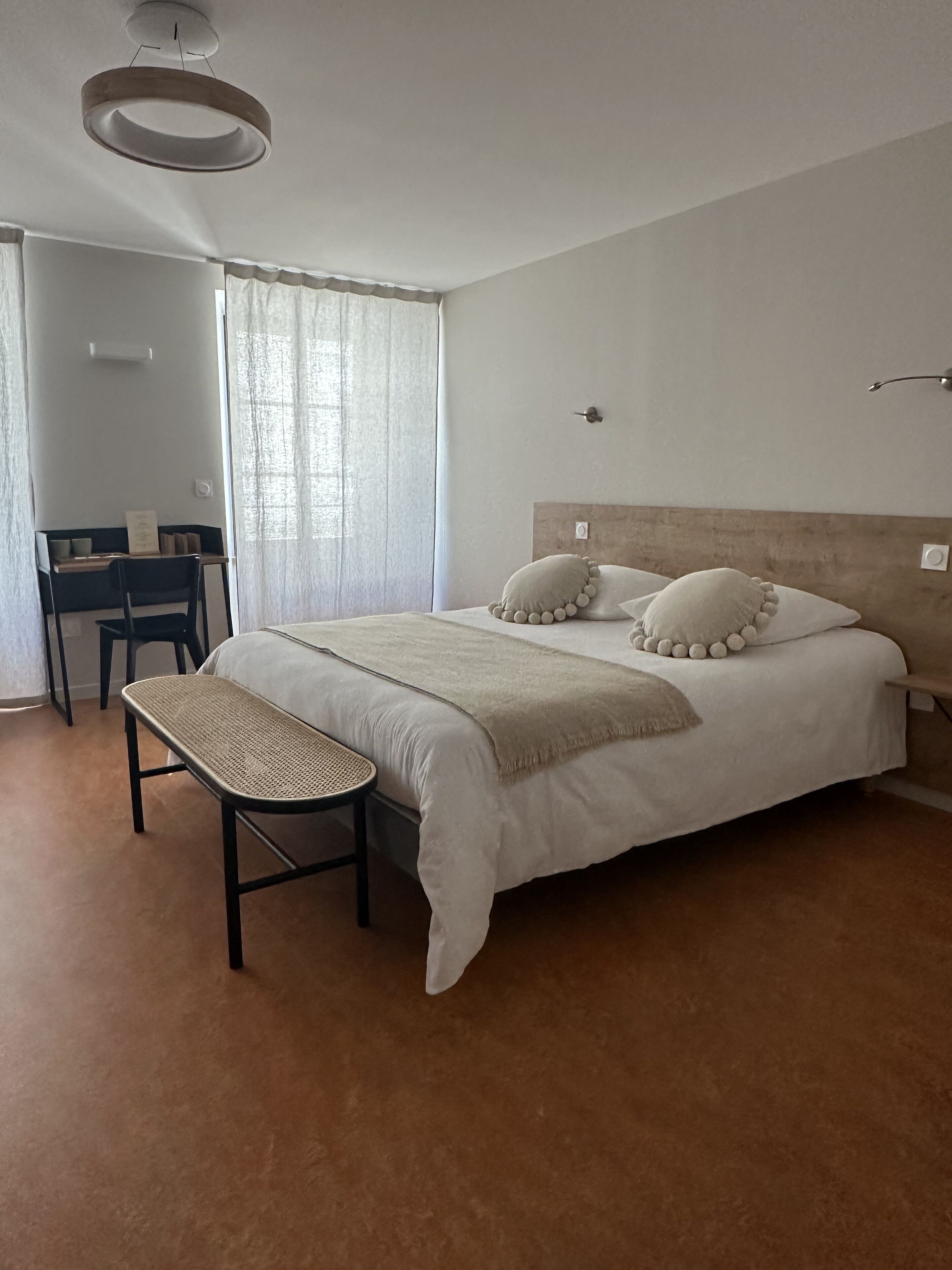 A bedroom with a bed, a bench, a desk, and a window with curtains.
