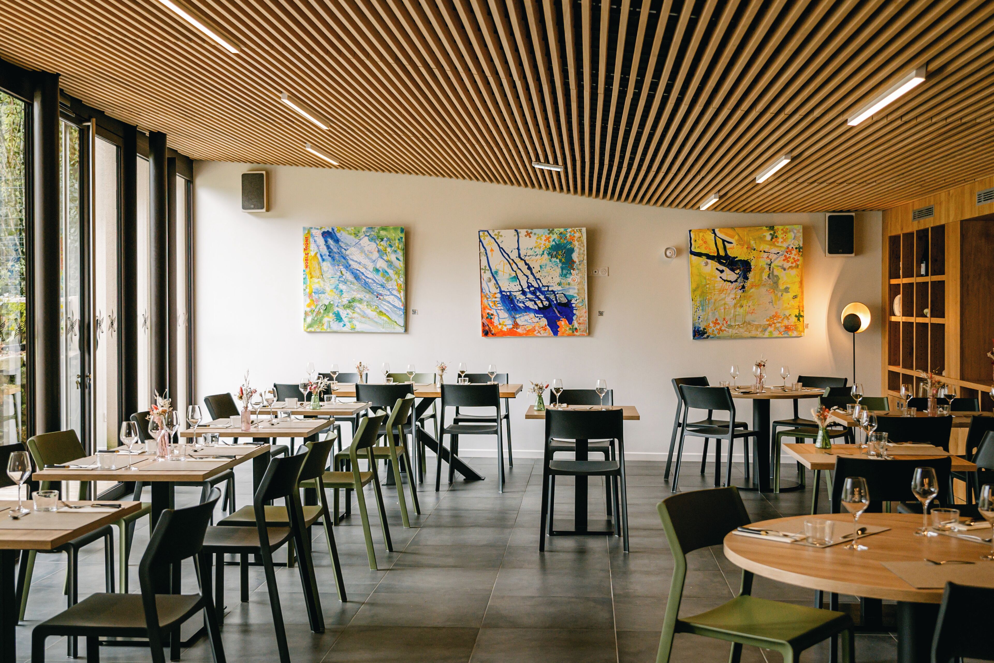 Ein modernes Restaurant mit Holzbalkendecke, großen Fenstern und abstrakter Kunst an den Wänden.