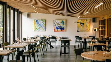 Ein modernes Restaurant mit Holzbalkendecke, großen Fenstern und abstrakter Kunst an den Wänden.