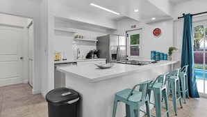 Een moderne keuken met een centraal eiland, barkrukken, een afvalbak en uitzicht op de omgeving.
