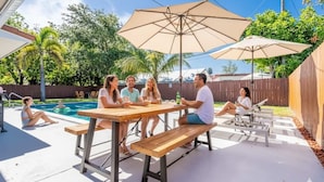 Een terras met een zwembad, houten tafels en parasols.