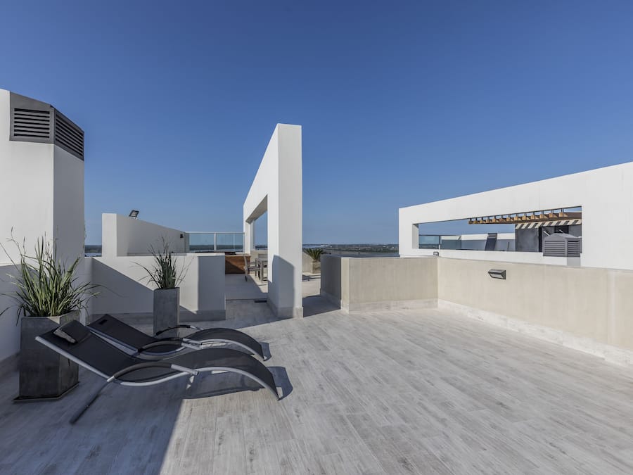 Una terraza en la azotea con sillones de descanso, plantas en macetas y vista al mar.