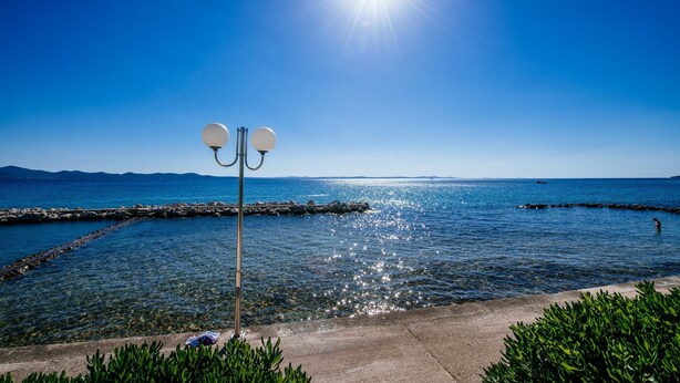 A clear blue sky, calm sea, and a concrete walkway with a street lamp. - Villa Sonik (Zadar)