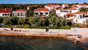 A coastal residential area with houses featuring red-tiled roofs, clear waters, and a stone wall. - Villa Sonik (Zadar)