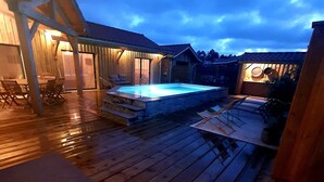 Eine Holzterrasse mit Whirlpool, Sitzgelegenheiten im Freien und einem überdachten Bereich mit Tisch und Stühlen.