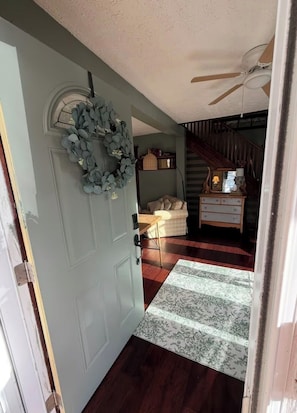 Um corredor com uma porta azul clara, uma grinalda, uma escada, um abajur e um tapete estampado.