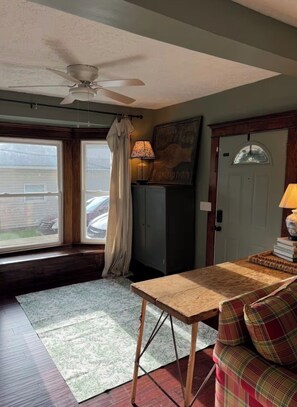 A room with a ceiling fan, a window with curtains, a table, a sofa, and a cabinet.