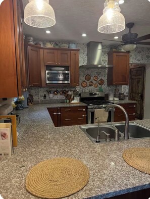 A kitchen with granite countertops, wooden cabinets, stainless steel appliances, and decorative wall tiles.