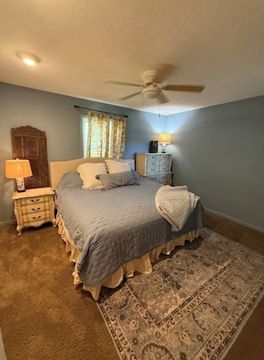A bedroom with a bed, a nightstand, a dresser, a ceiling fan, and a patterned rug.