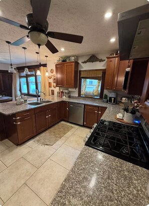 A kitchen with granite countertops, wooden cabinets, a gas stove, and a ceiling fan.
