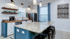 A kitchen with a central island, wooden shelves, a refrigerator, and pendant lights.