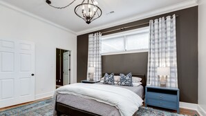 A bedroom with a bed, two nightstands, a chandelier, and a large window with curtains.