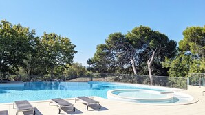 Une piscine dotée de chaises longues et d’un petit espace avec un jacuzzi, le tout entouré d’arbres et délimité par une clôture en métal.