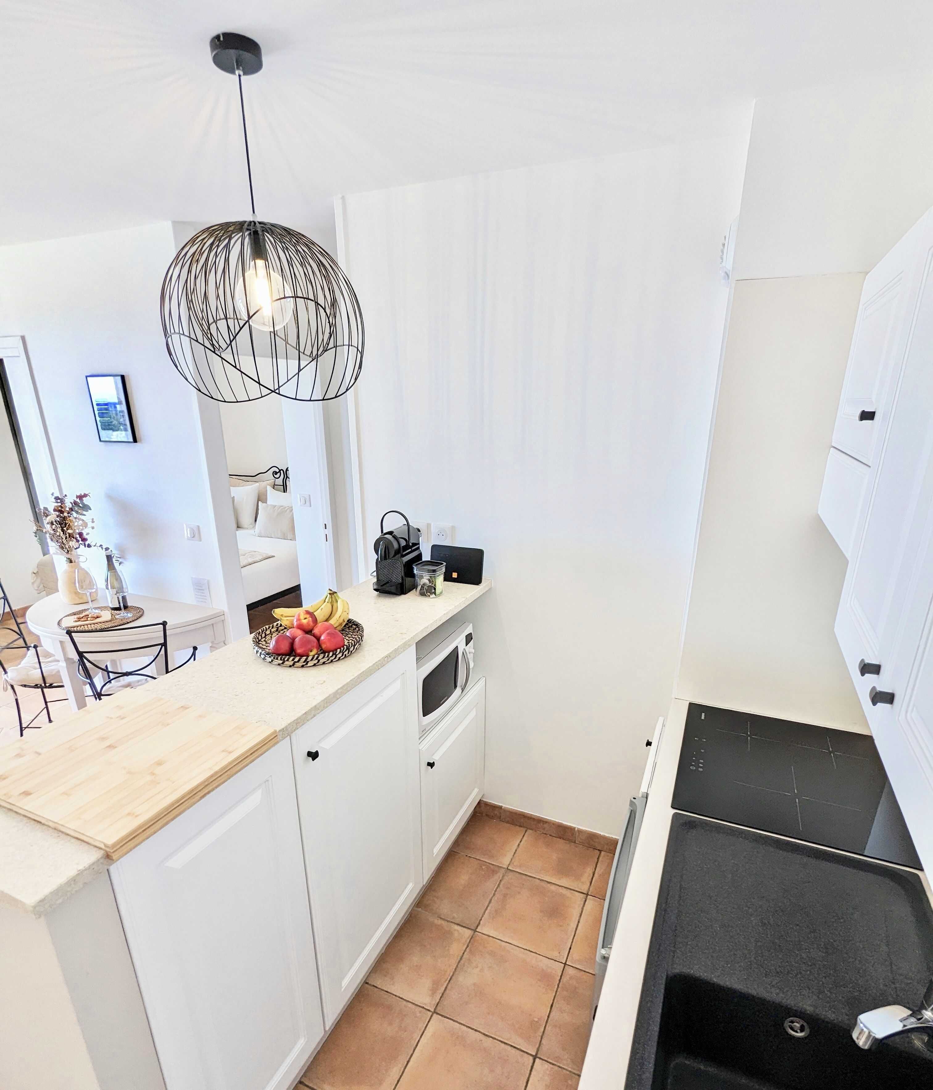A compact kitchen with white cabinets, a wooden countertop, a black stove, and a hanging light fixture.