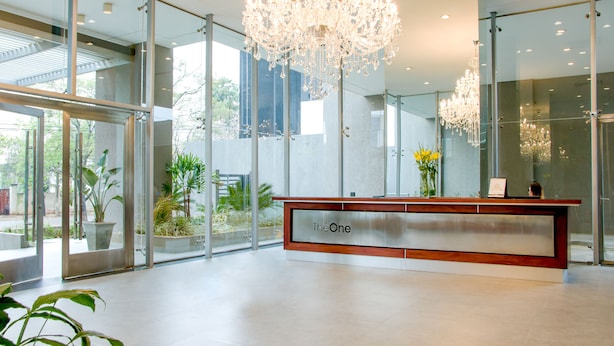 A modern reception area with a glass facade, a wooden reception desk labeled "The One," and a large chandelier. - Asuncion Rent Suites Santa Teresa (Asunción)