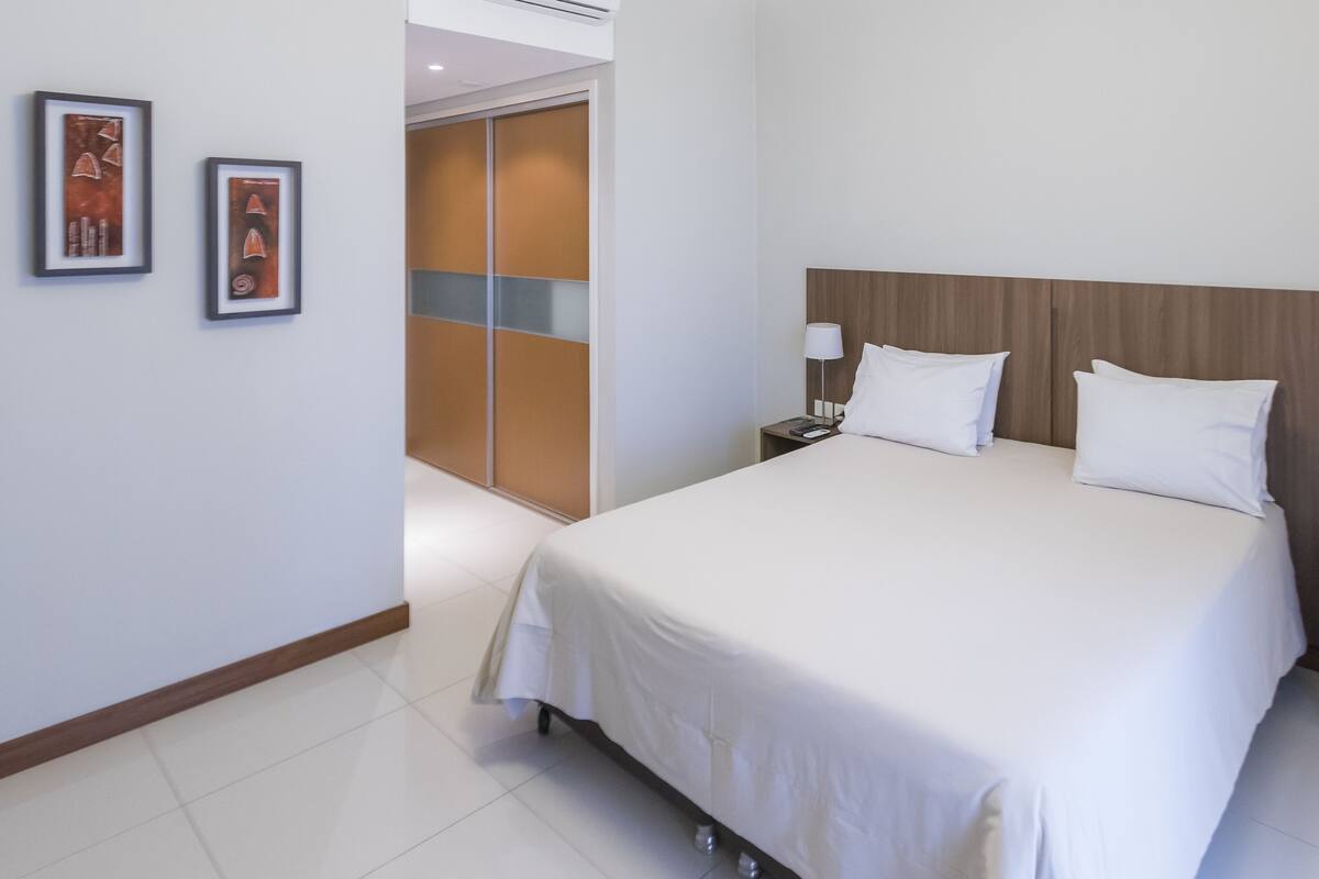 A hotel room with a large bed, two bedside tables, a wardrobe, and two framed pictures on the wall.