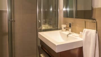 Un baño moderno con ducha envuelta en cristal, un lavabo blanco y un espejo grande.