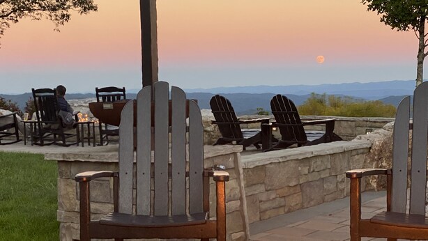 Espace extérieur aménagé avec des chaises et un foyer, le tout offrant une vue imprenable sur les montagnes et un magnifique coucher de soleil.