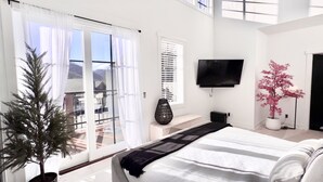 Une chambre avec un lit, une télévision, une plante en pot et un balcon avec vue.