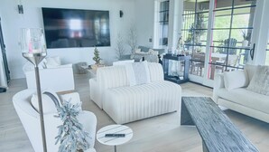 Un salon moderne avec un grand téléviseur à écran plat, des canapés blancs, une table basse et un sapin de Noël.