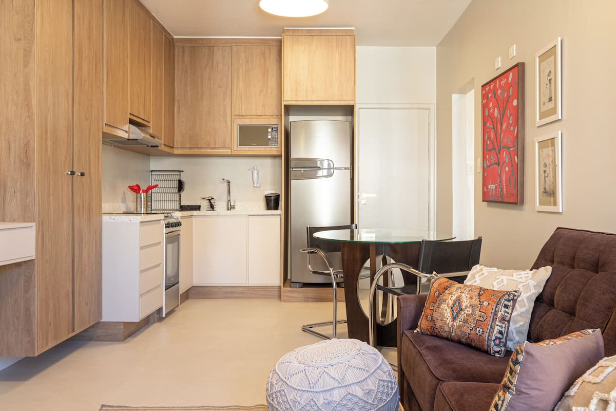 Een moderne keuken met houten kastjes, een roestvrijstalen koelkast en een eethoek met een glazen tafel en stoelen.