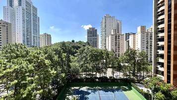 Una cancha de tenis rodeada de edificios residenciales altos y abundante vegetación.