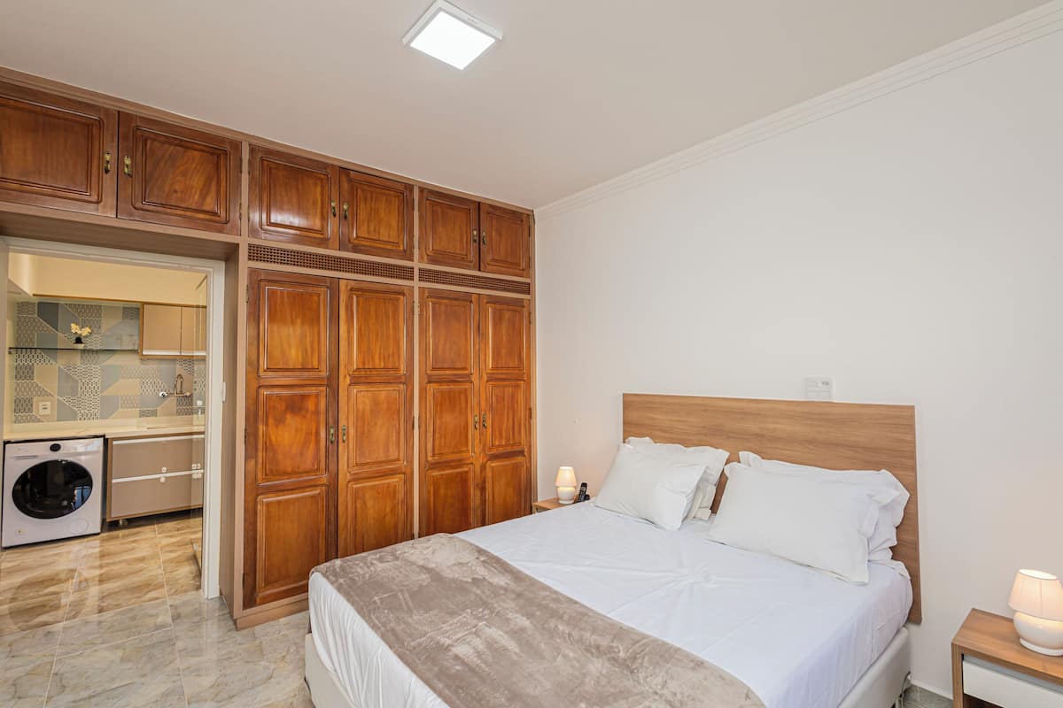 Een slaapkamer met een bed, een houten garderobe en een wasmachine.