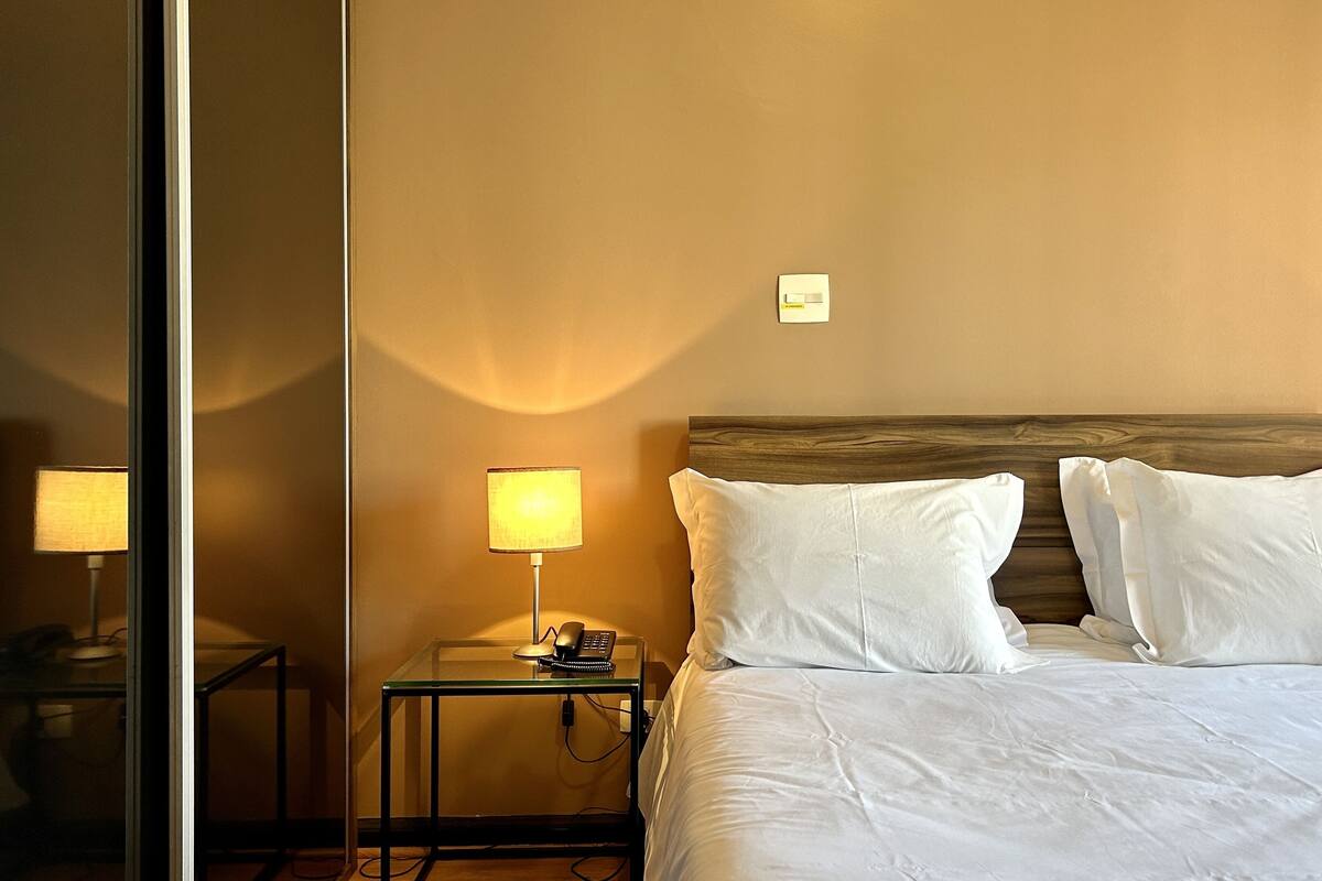 Een hotelkamer met een bed, een nachtkastje met een lamp en een spiegel.