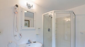 Un baño con lavamanos blanco, espejo, secador de pelo y ducha con mampara de vidrio.