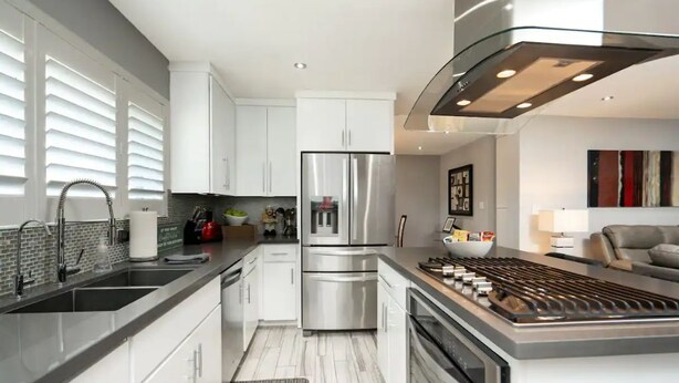 Une cuisine moderne avec des meubles blancs, des appareils en acier inoxydable et un îlot central doté d’une plaque de cuisson.