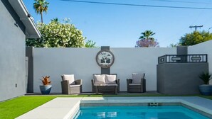 Une piscine agrémentée de deux fauteuils en osier et d’une œuvre d’art décorative fixée au mur.