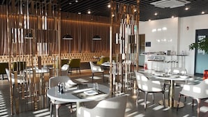 Un restaurant moderne avec des tables rondes, des chaises vertes et un paravent décoratif en bois.
