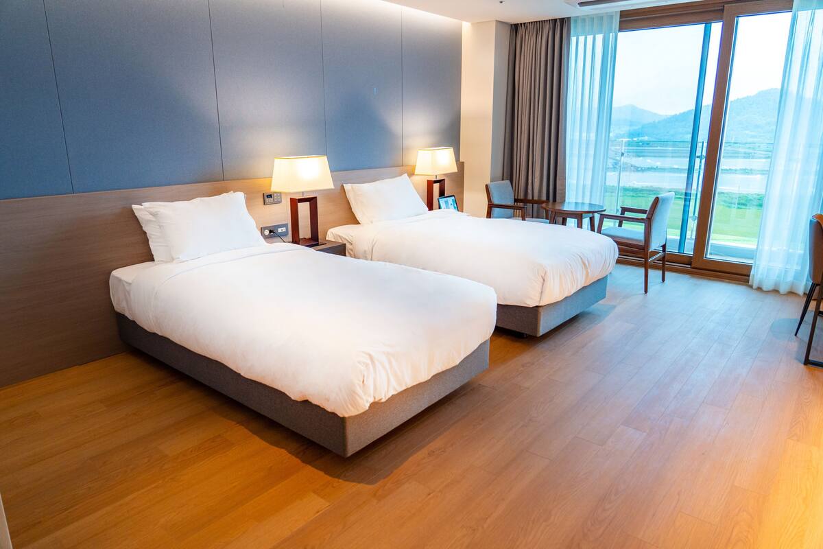 Habitación de hotel con dos camas, un escritorio, una silla y un ventanal con vistas.