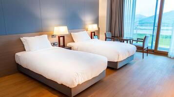 Habitación de hotel con dos camas, lámparas de noche, una silla, una mesita y vistas a un paisaje a través de amplias ventanas.