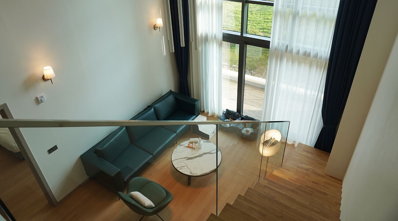 A modern living room with a green sofa, a round coffee table, and a glass railing overlooking a wooden floor.