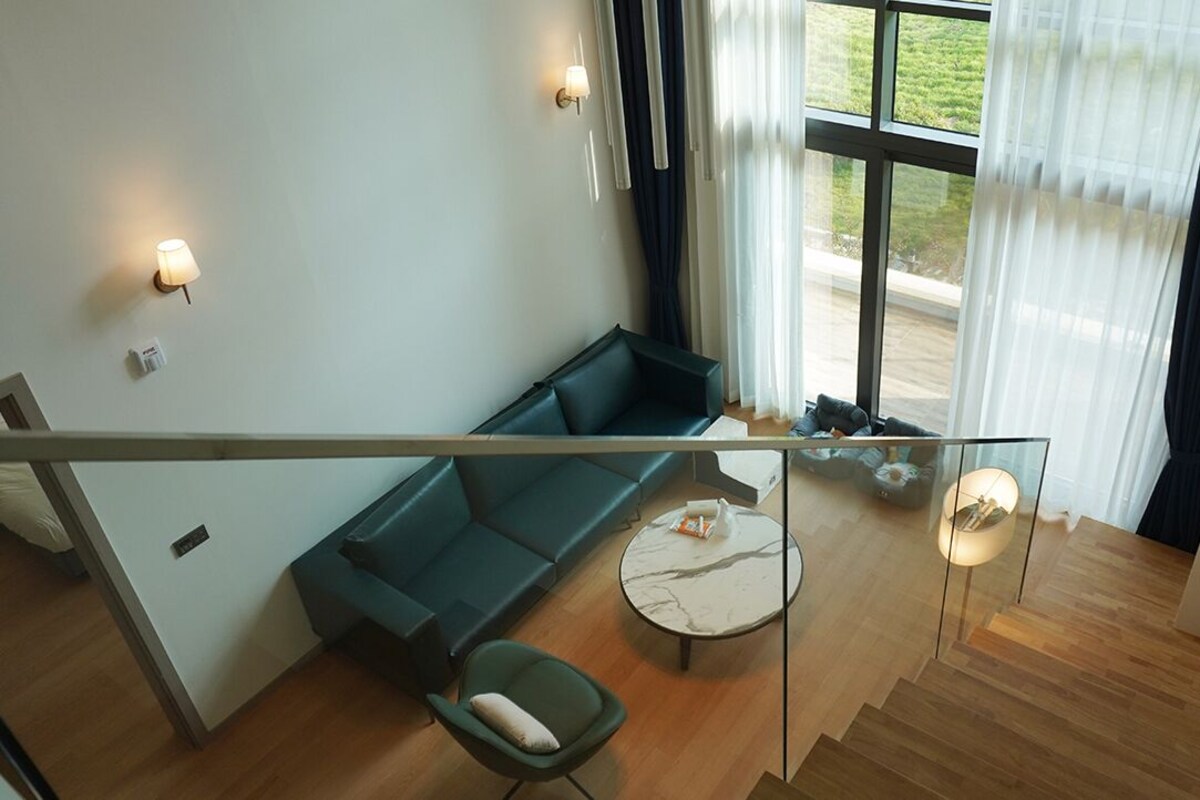 A modern living room with a green sofa, a round coffee table, and a glass railing overlooking a wooden floor.