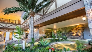 Un hall d’hôtel agrémenté d’un élément décoratif central avec de l’eau, de plantes tropicales et un mur en pierre en arrière-plan.