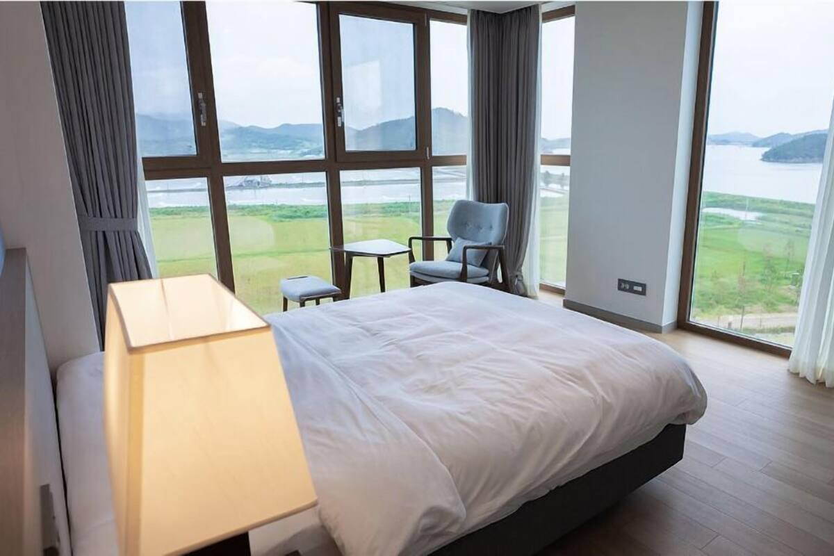 Habitación de hotel con una cama grande, un escritorio, una silla y vistas a un lago y montañas.