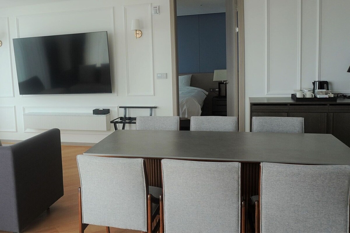 Una sala de estar moderna con un televisor de pantalla plana, un sofá gris y un comedor con mesa y sillas.
