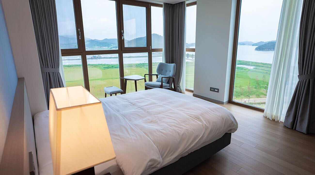 Une chambre d’hôtel avec un grand lit, une table de chevet, une chaise et une vue sur un lac et des montagnes.