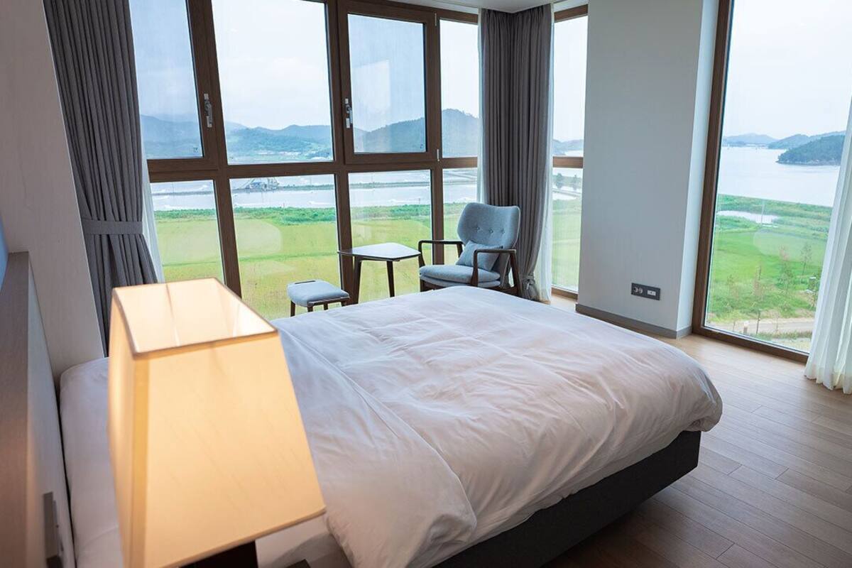 Habitación de hotel con una cama grande, una mesita de noche, una silla y vistas a un lago y montañas.