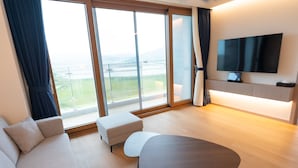 Une chambre d’hôtel moderne, dotée d’un canapé, d’une petite table, d’un téléviseur et d’une grande fenêtre donnant sur l’extérieur.