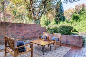 Une terrasse avec des meubles en bois, un mur en briques et un jardin en arrière-plan.
