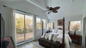 Camera da letto con letto a baldacchino, ventilatore a soffitto e vista su un pontile in legno attraverso ampie porte scorrevoli in vetro.