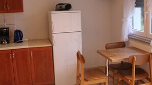 Une cuisine compacte avec des meubles en bois, un réfrigérateur blanc, une machine à café et un téléviseur à écran plat fixé au mur.
