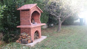 Une cheminée extérieure en briques, dotée d’une cheminée, entourée de verdure et d’un arbre.