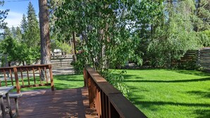 Eine Holzterrasse mit Metallgeländer, die zu einer Rasenfläche mit Bäumen und einer Steinmauer im Hintergrund führt.