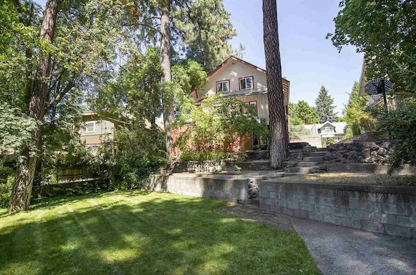Situated in a lush green setting, this two-story house features a prominent roof and white trim, surrounded by mature trees and a well-maintained lawn.